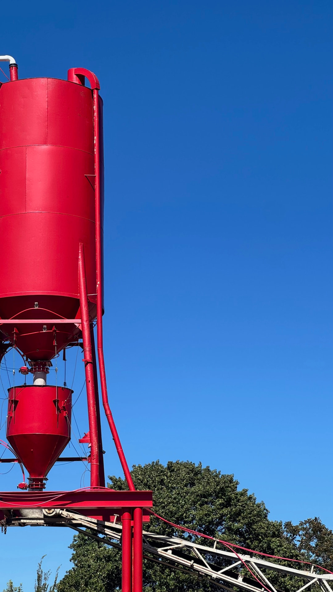 Red concrete batch plant silo against a clear blue sky at the future Readyline Redi-Mix plant site on OK-9 in Eufaula